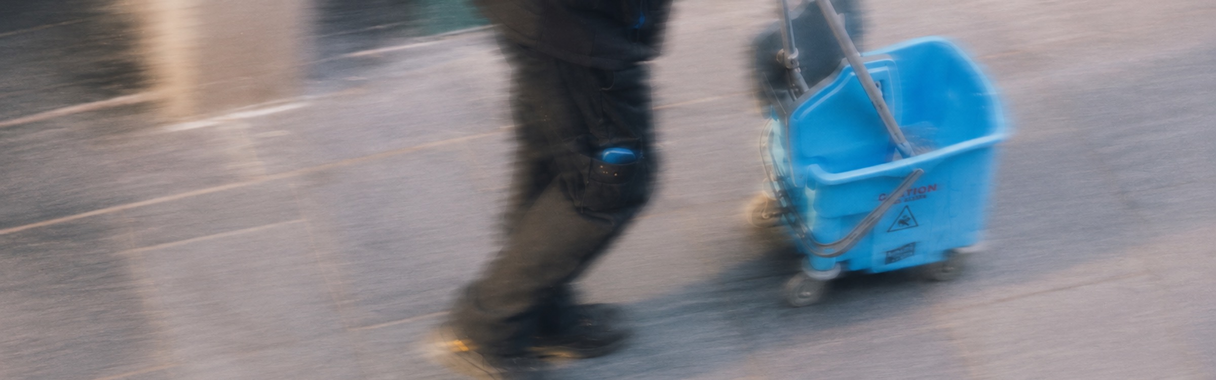 A person pushing a cleaning cart across a tiled floor